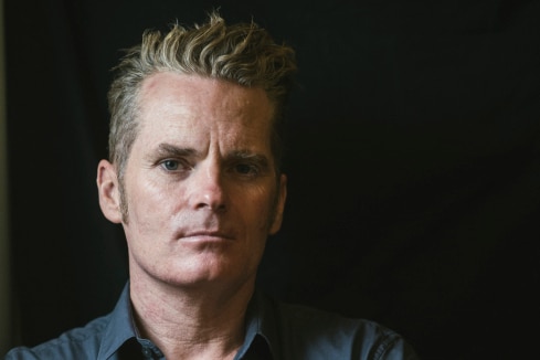 Author James Bradley stands with his arms crossed against a black background.