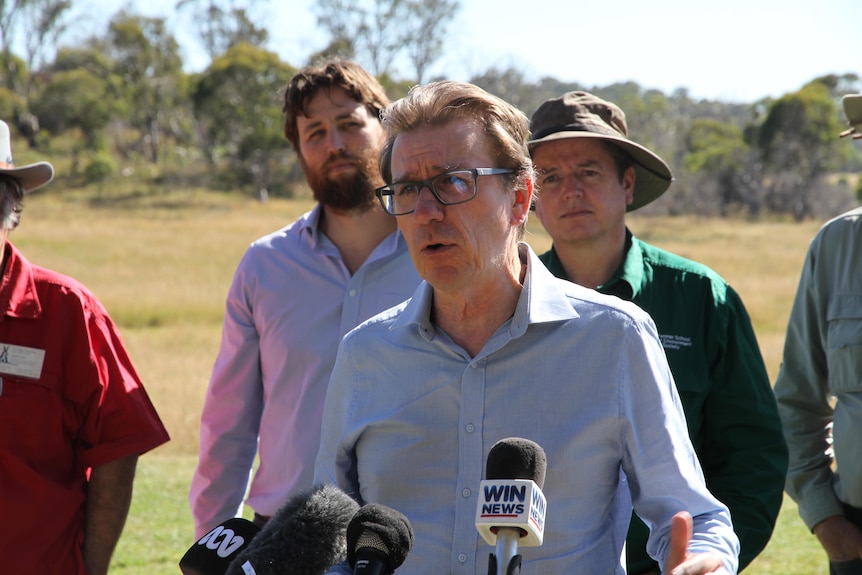 A male politician speaks into a mic surrounded by four other men
