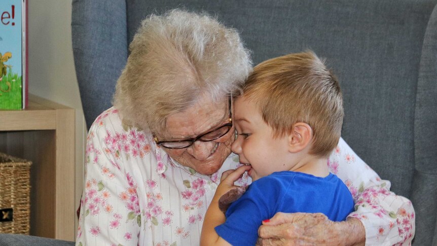 An elderly woman smiles as she hugs a young boy.