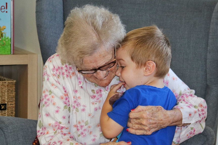 An elderly woman smiles as she hugs a young boy.