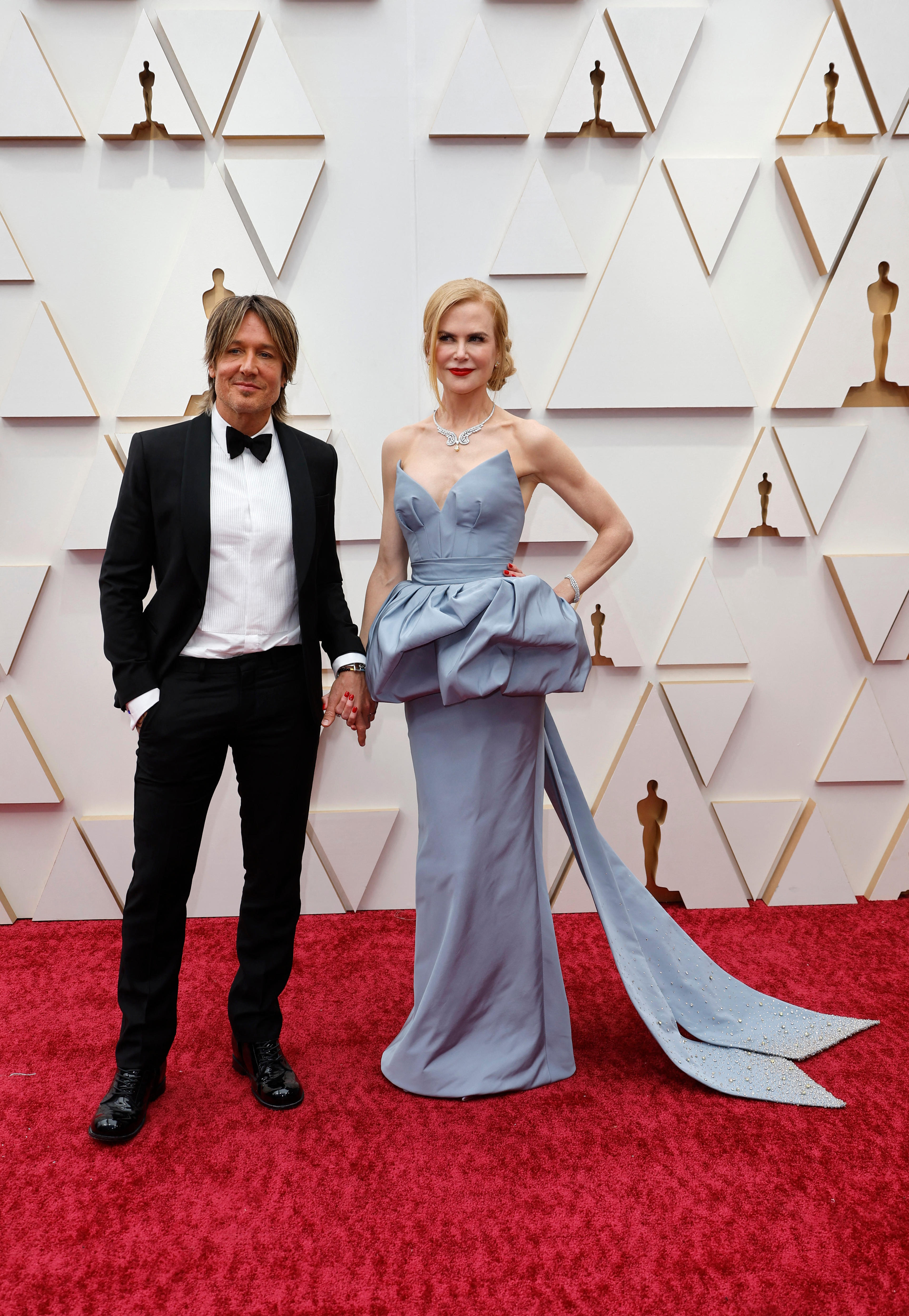 keith urban andn icole kidman stand holding hands on the oscars red carpet, nicole wearing a grey-blue down with a bell waist