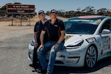A husband and wife racing team posing with their car at the 90-Mile Straight on the Nullarbor.  