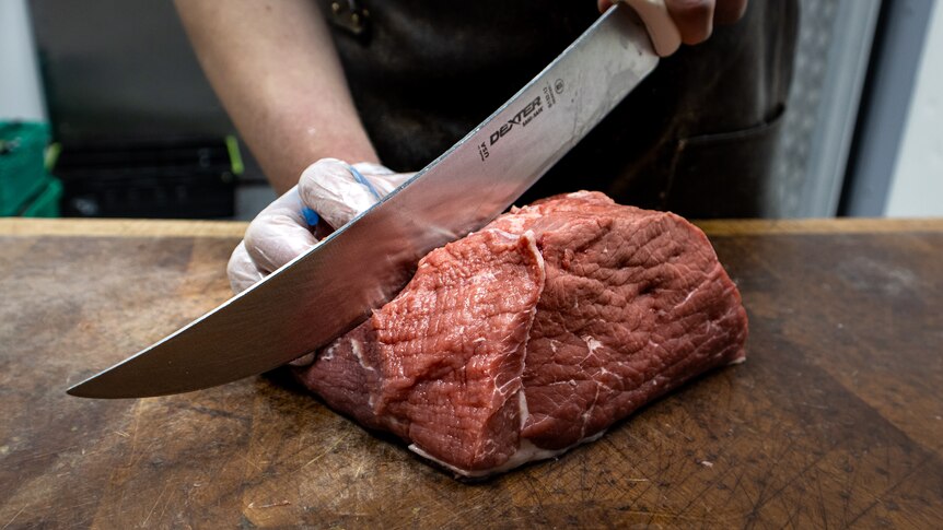 A gloved hand slices through the middle of a silverside roast with a bit knife