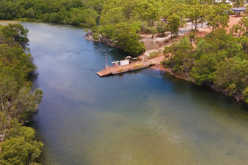 A wide green river surrounded by dry trees.  ferry is at the edge of the river