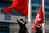 Soldiers stand by flag poles with both the Chinese (red with yellow stars) and Hong Kong (red with a white flower) flags flying