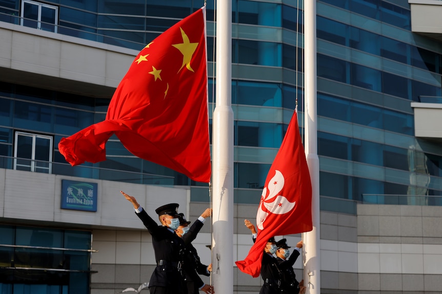 Soldiers stand by flag poles with both the Chinese (red with yellow stars) and Hong Kong (red with a white flower) flags flying