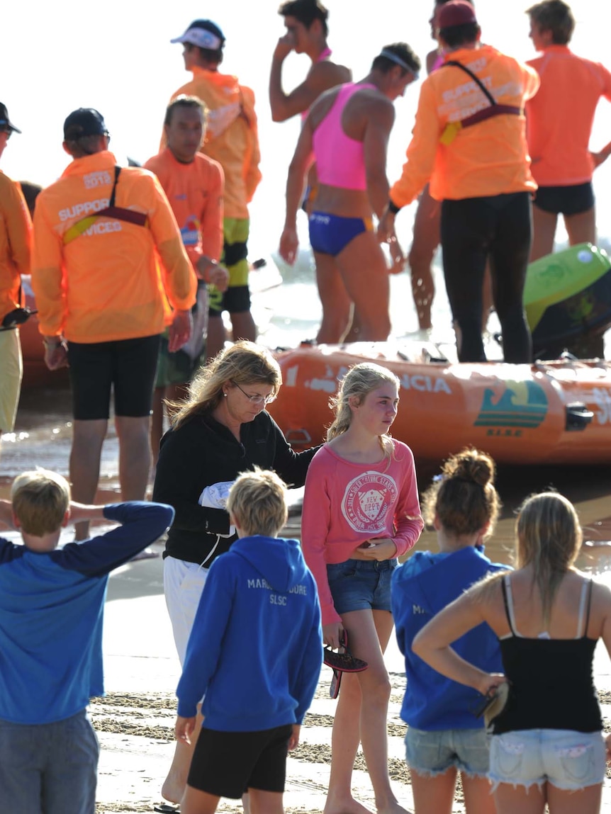 Family members of 14-year-old Matt Barclay walk along Kurrawa beach amid life savers and competitors