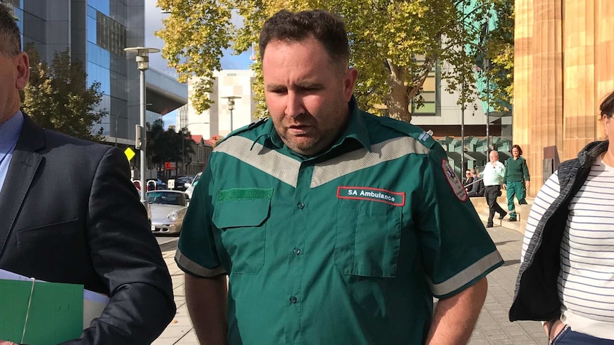 A man in an SA Ambulance uniform on a city street.