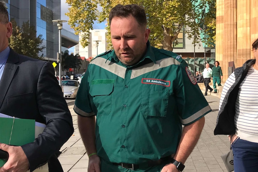 A man in an SA Ambulance uniform on a city street.