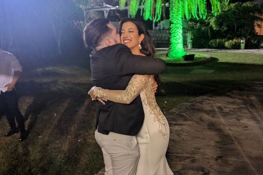 Veton Musai and Lindita Musai hug each other outside with a large palm tree behind them.