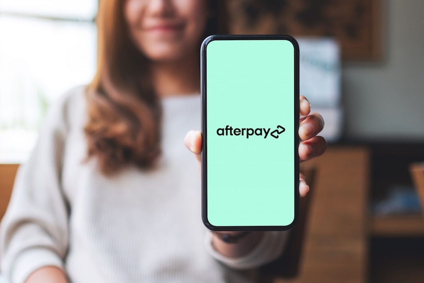 The woman holds an iPhone in her left hand, displaying the Afterpay name and logo.