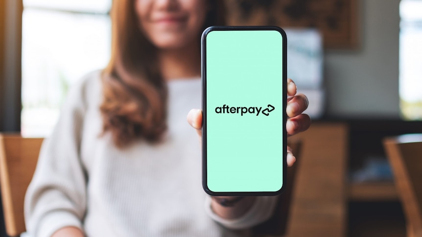 A woman holds up an iPhone with the mint green Afterpay logo on its screen.
