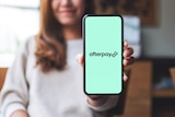 A woman holds an iPhone in her left hand showing the Afterpay name and logo.