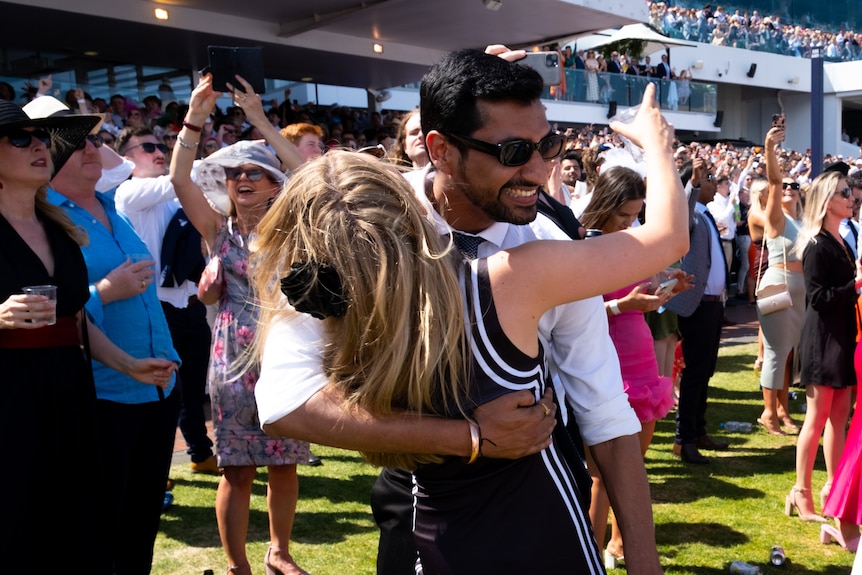 A man and woman embrace and smile in the crowd at the 2023 Melbourne Cup.