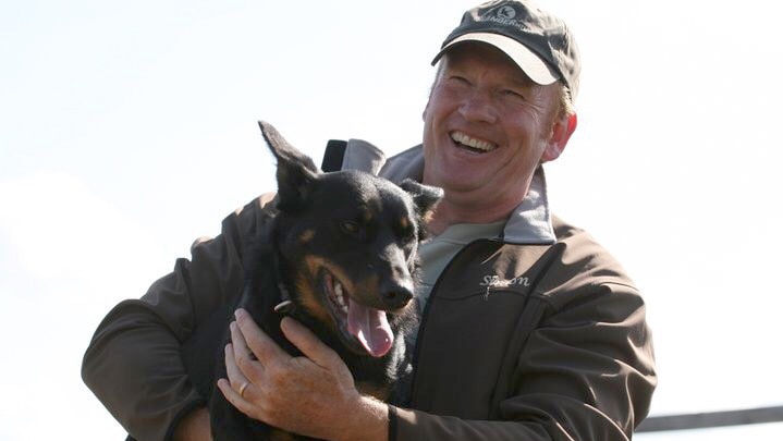 A smiling man cuddling a large black dog.