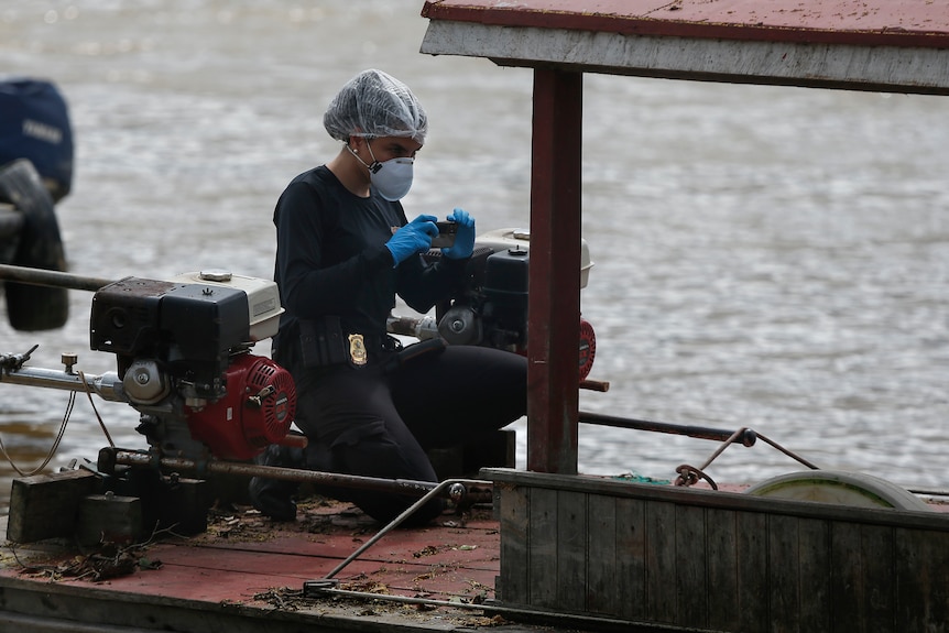 A police officer with her badge displayed on her jeans kneels on a rusted boat, photographing something out of frame