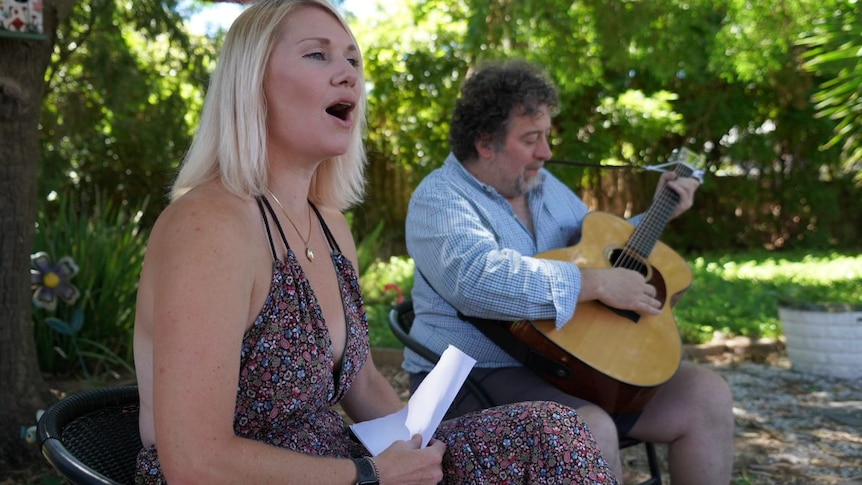 A woman singing as a man plays a guitar in an outdoor setting
