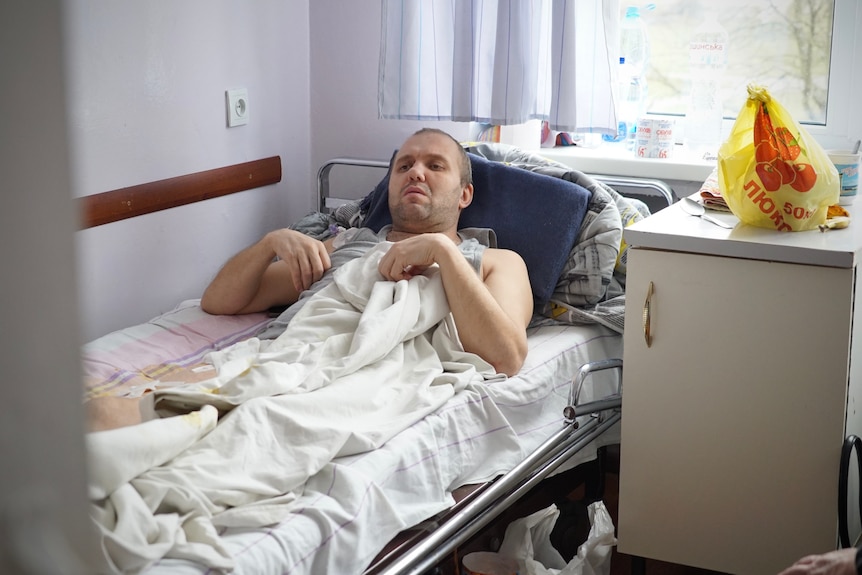 A young man lies in a hospital beg with a leg wound.