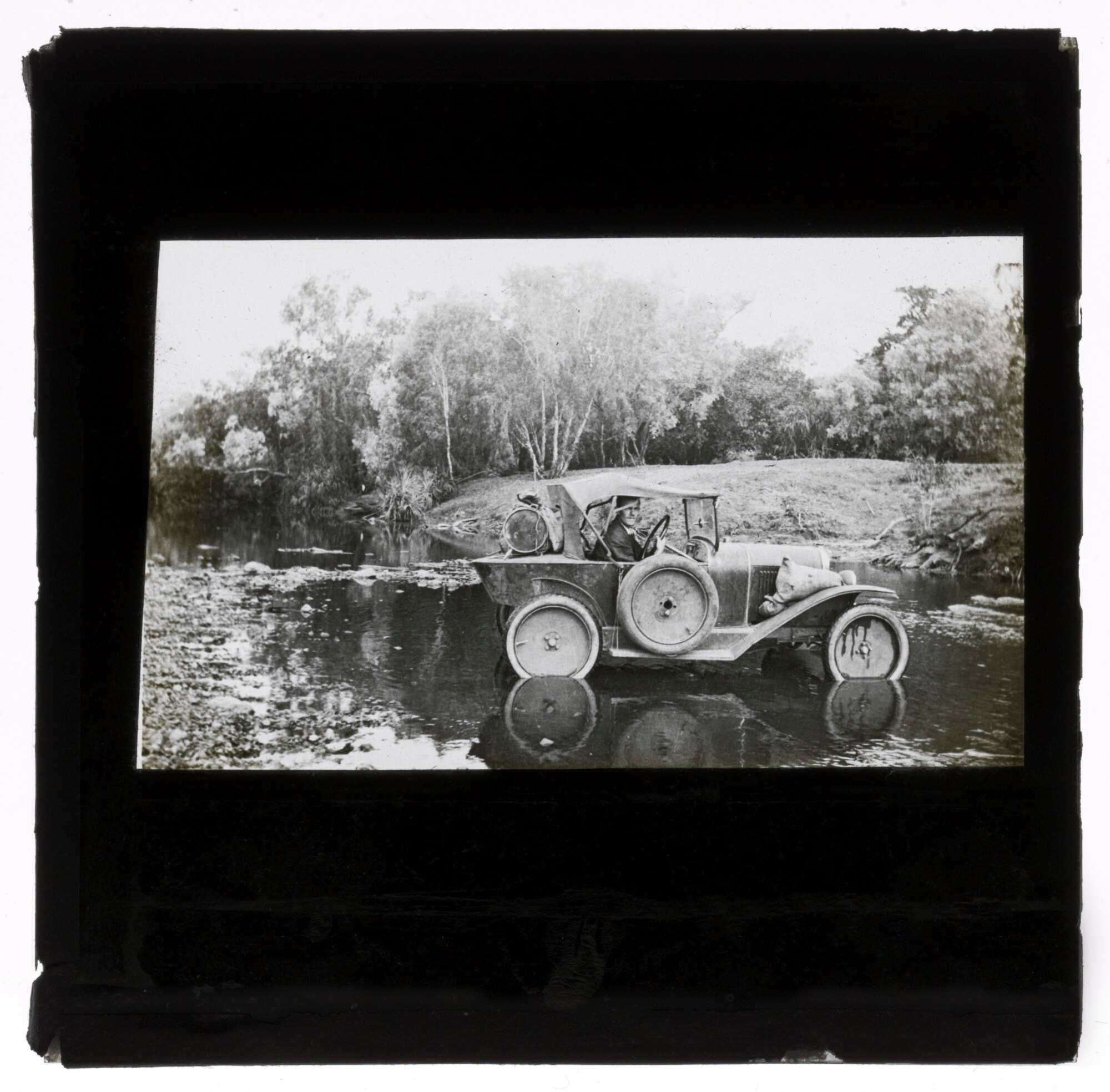 A black-and-white photograph of a car stuck in a few inches of river with Nevill Westwood driving