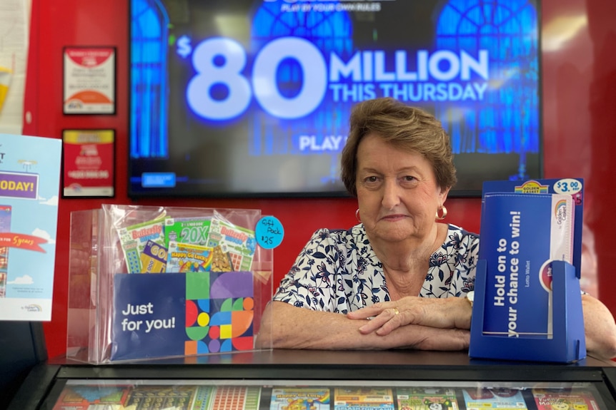 Woman standing at newsagent counter with a $80-million lottery sign in background.
