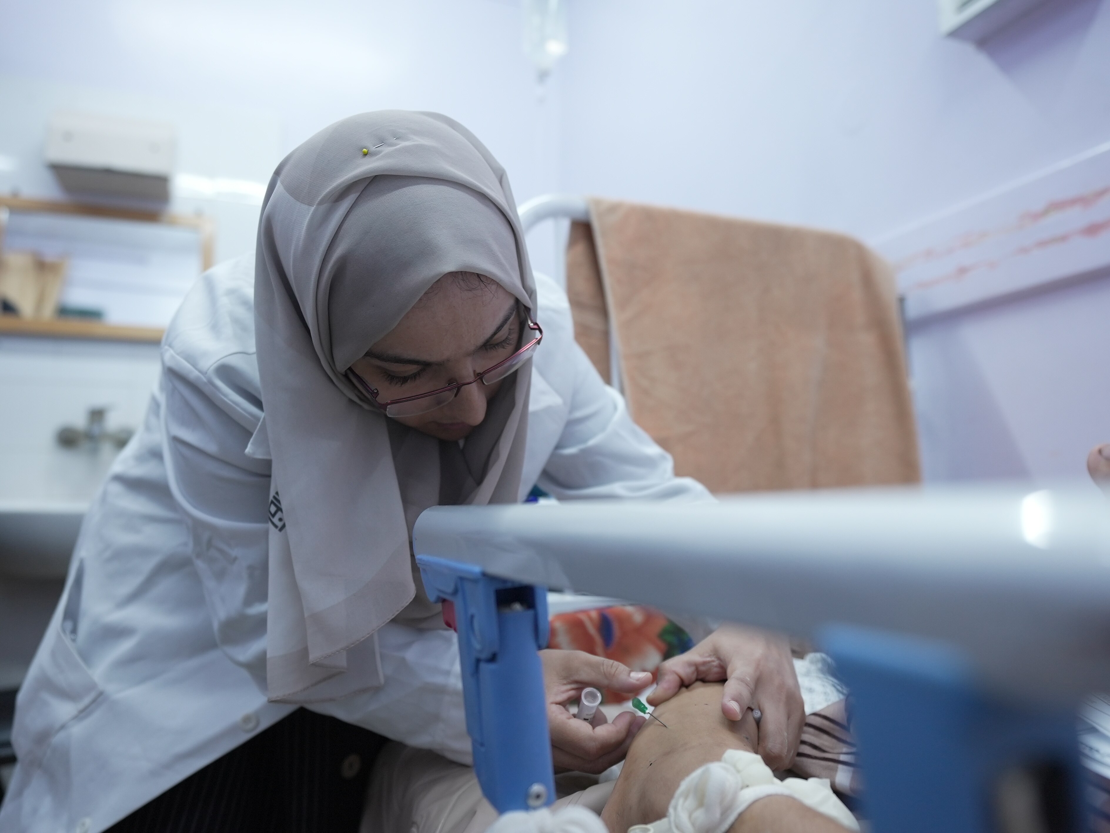 A female nurse wearing a hijab is seen administering an IV on a patient in Gaza.