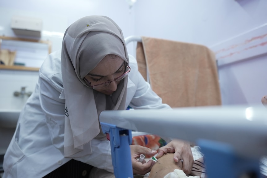 A female nurse wearing a hijab is seen administering an IV on a patient in Gaza.