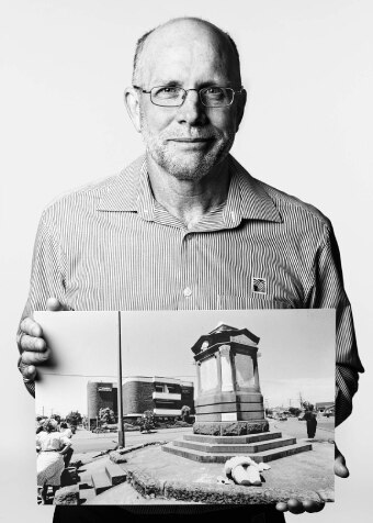 A man posing for a portrait holding an historic photograph.