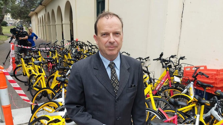 A man looks at the camera, with a large pile of bikes behind him.