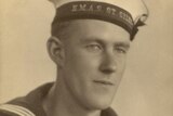 A man in a HMAS St Giles naval cap sits for a 1940s studio portrait.