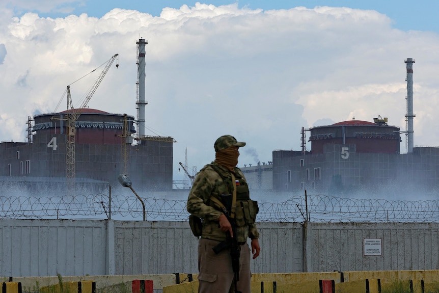 Солдат с российским флагом на форме стоит возле Запорожской атомной электростанции.
