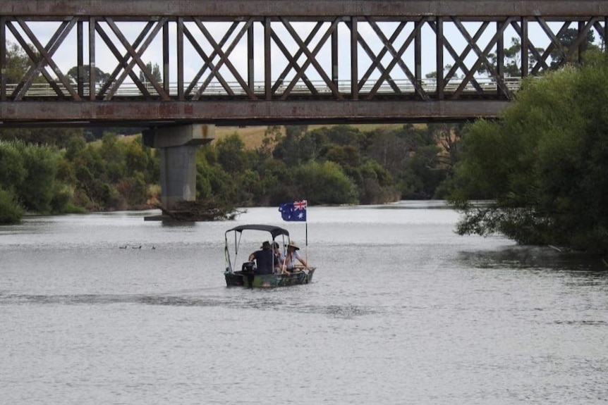 Pople on a boat on a river near old railway bridge.