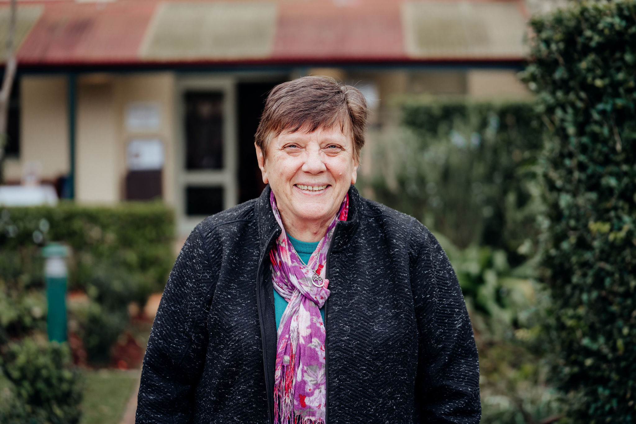 A woman wearing a black jacket standing outside a building and garden