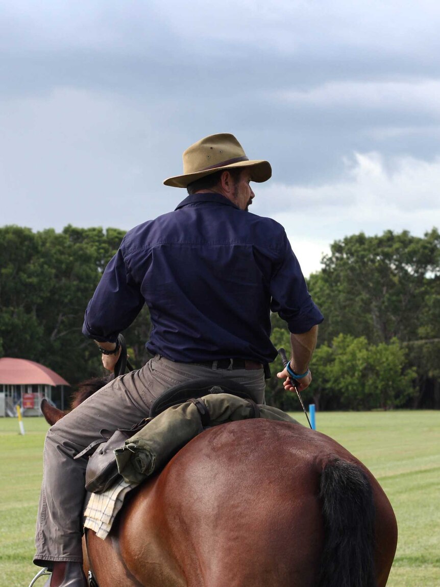A man in a hat sits astride a brown horse in a field.