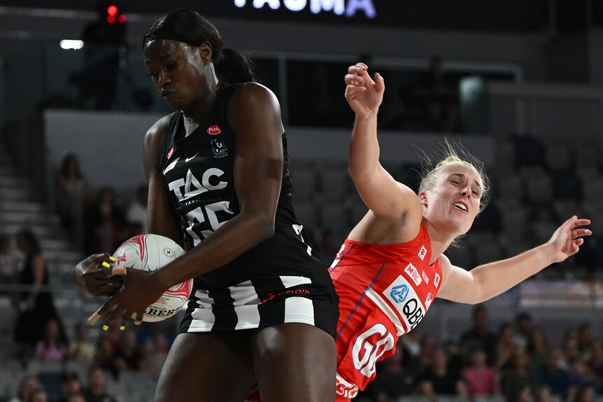 A Collingwood Magpies Super Netball player holds the ball in front of a NSW Swifts opponent.