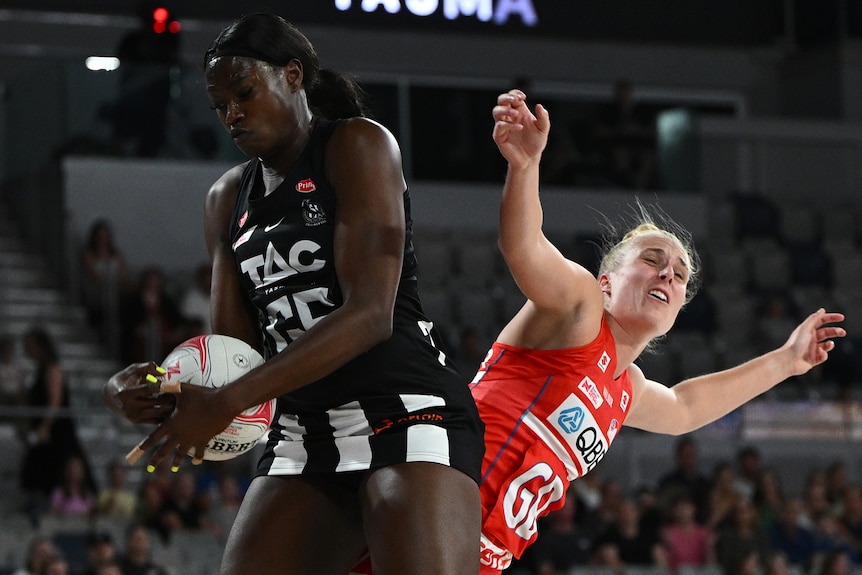 A Collingwood Magpies Super Netball player holds the ball in front of a NSW Swifts opponent.
