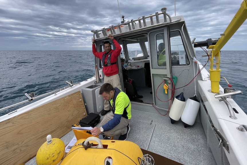 Researchers use computer equipment attached to a seismometer on the deck of a boat. Dark clouds in the distance.