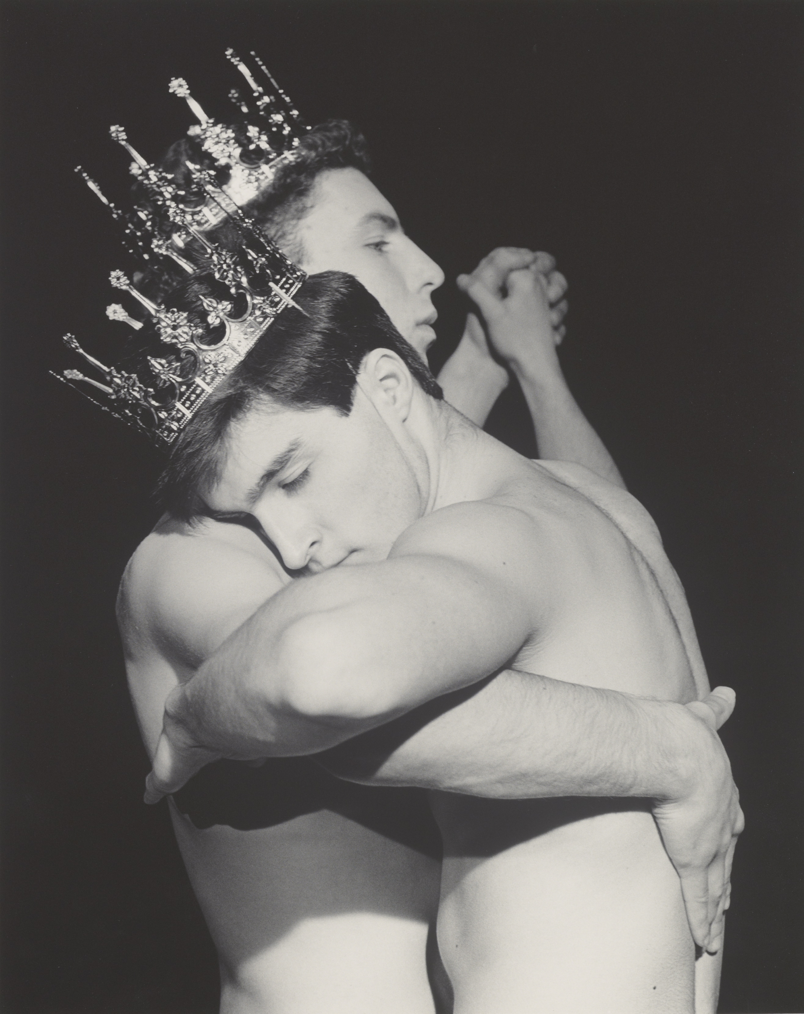 Black and white photograph of two muscular young men in a dancing pose, both wearing crowns.