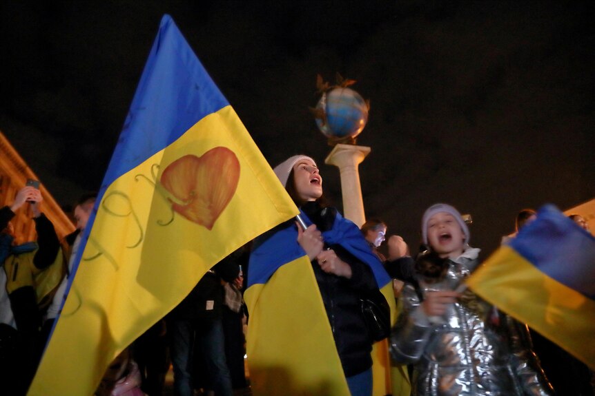 Perople carrying Ukrainian flags cheer and celebrate.