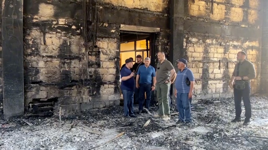 Men standing in burnt down synagogue. 
