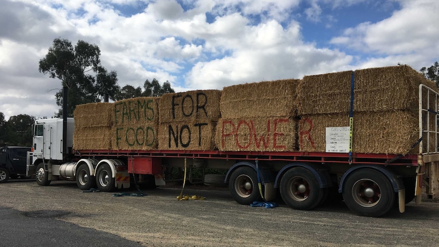 A truck carrying hay bails painted with the slogan "farms for food not power" is parked outside a community meeting in Culcairn