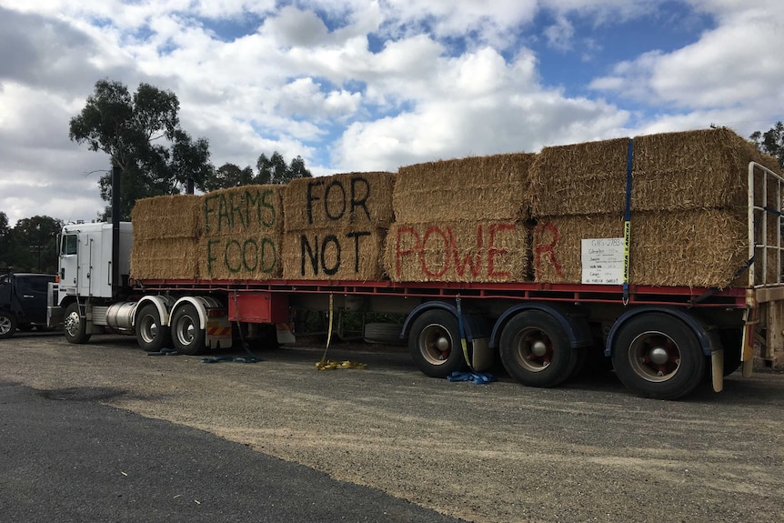 A truck carrying hay bails painted with the slogan "farms for food not power" is parked outside a community meeting in Culcairn