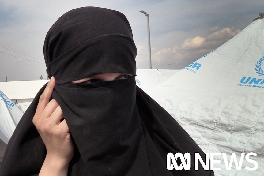 A woman in a hijab looks off while standing in a UNHCR refugee camp