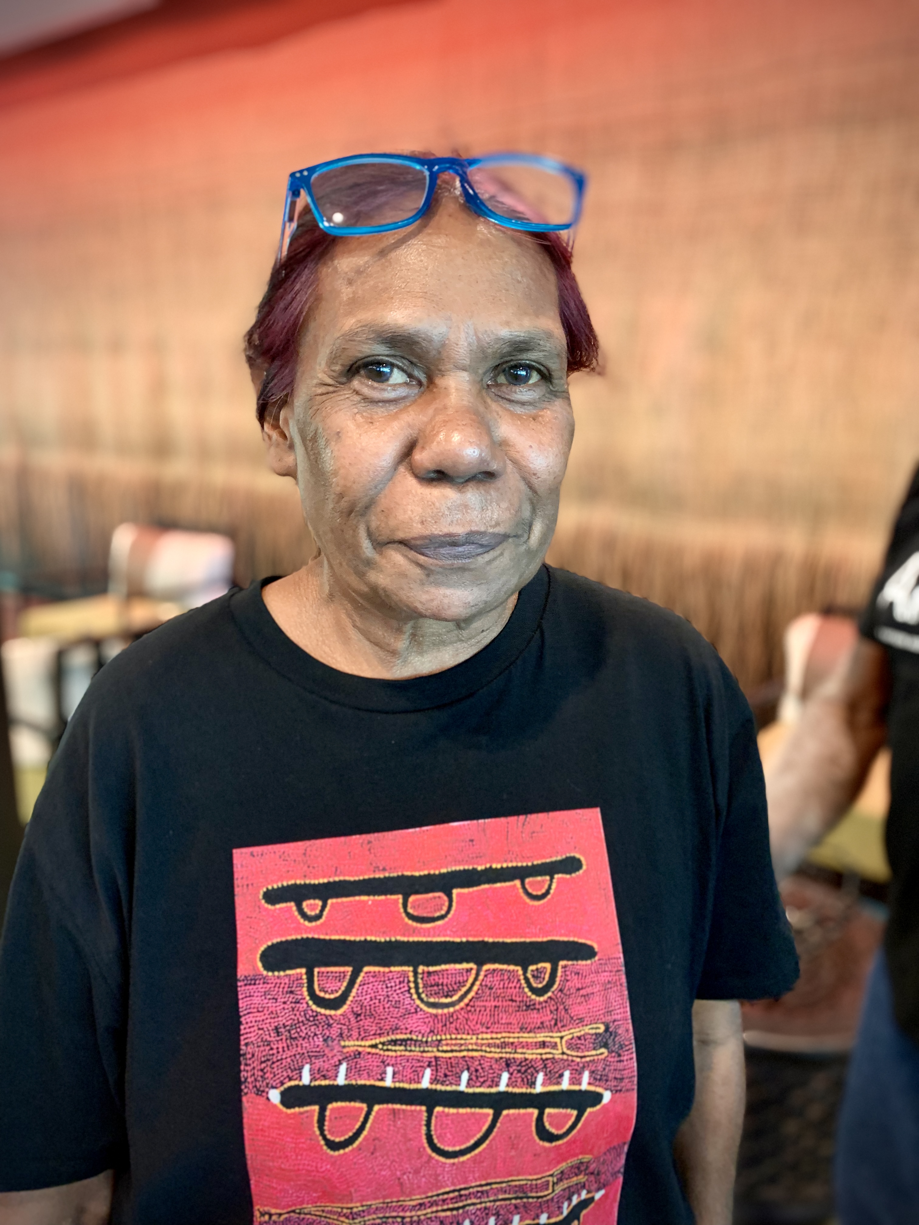 Indigineous artist Maxine Charlie wears a black and red t-shirt with blue glasses.