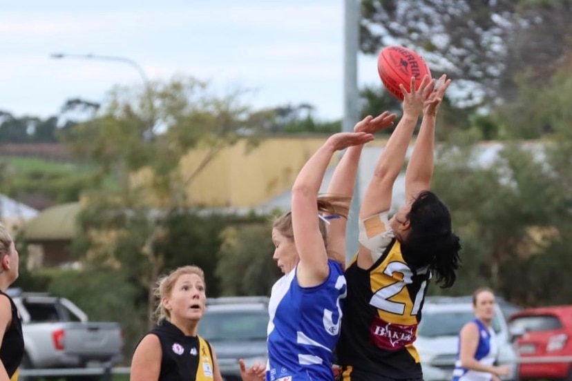 Three women jump up to contest a grab in a game of Australian Football.