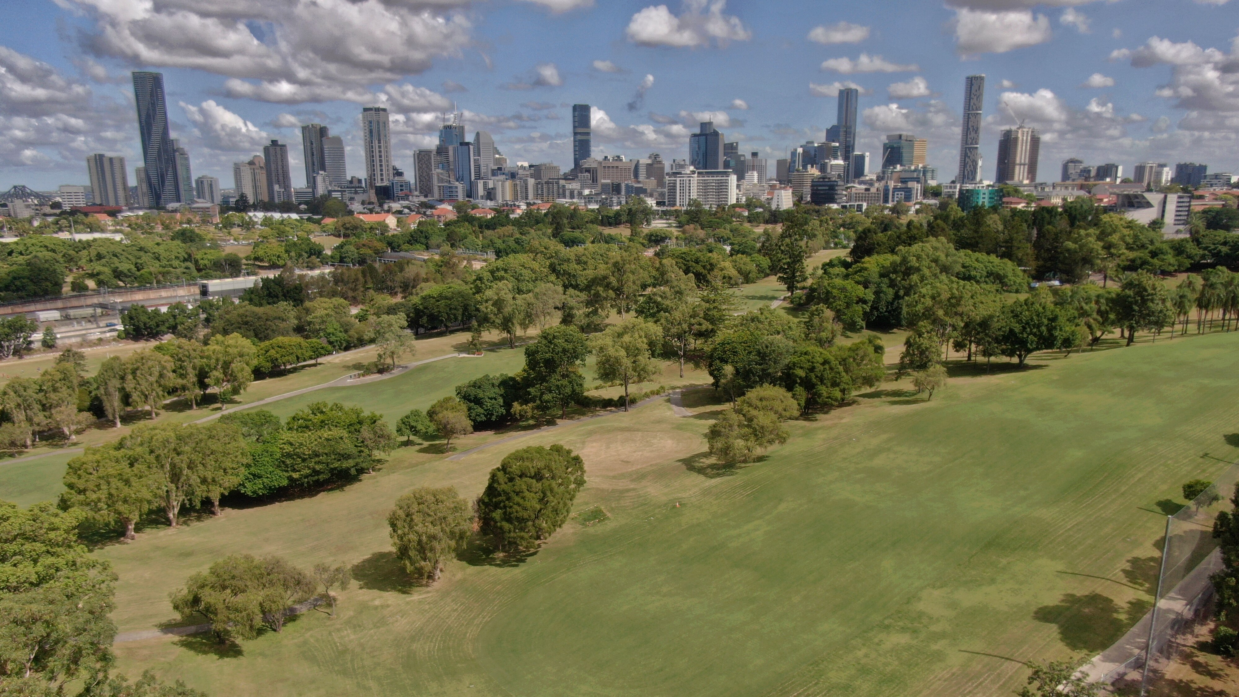 A grassy parkland dotted with trees and a city skyline in the background.