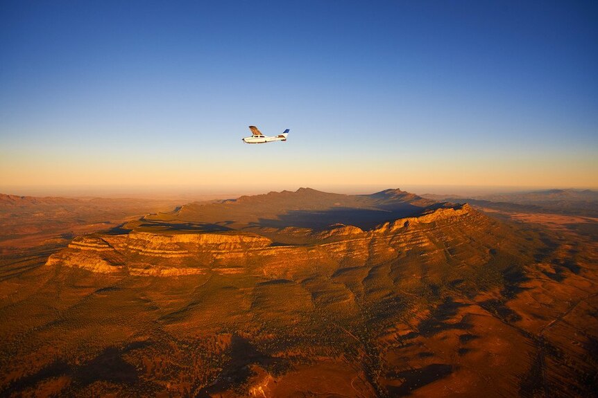 A white charter plane flies above land surrounded by a wall of mountains.