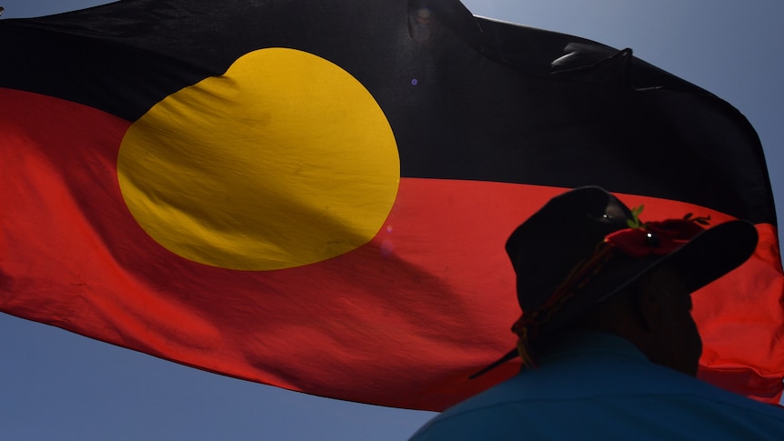 a person in an Akubra hat silhouetted against an Indigenous flag