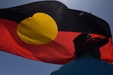 a person in an Akubra hat silhouetted against an Indigenous flag