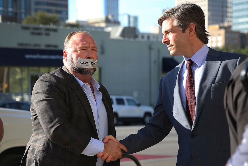 Alex Jones with tape on his mouth shaking hands with his lawyer Andino Reynal. 