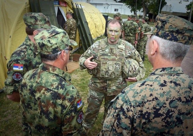 A man in military camouflage uniform speaking to three other army men